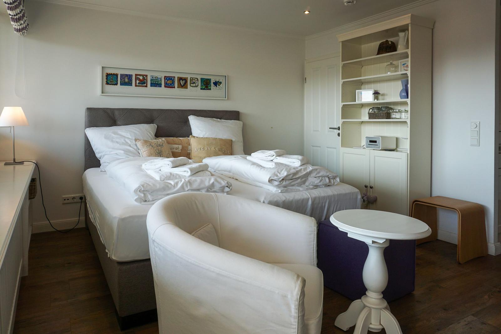 Zimmer mit Doppelbett, Sessel und Sideboard mit Regal