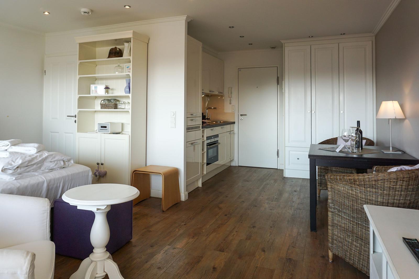 Wohnung mit Schlafzimmer, Küche und Essbereich. Holzboden und weiße Möbel.