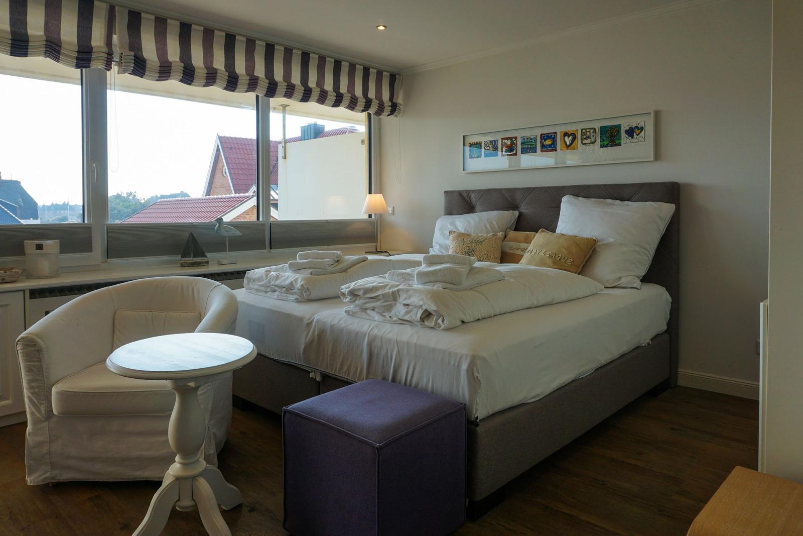 Schlafzimmer mit Bett, Sessel und Fensterblick
