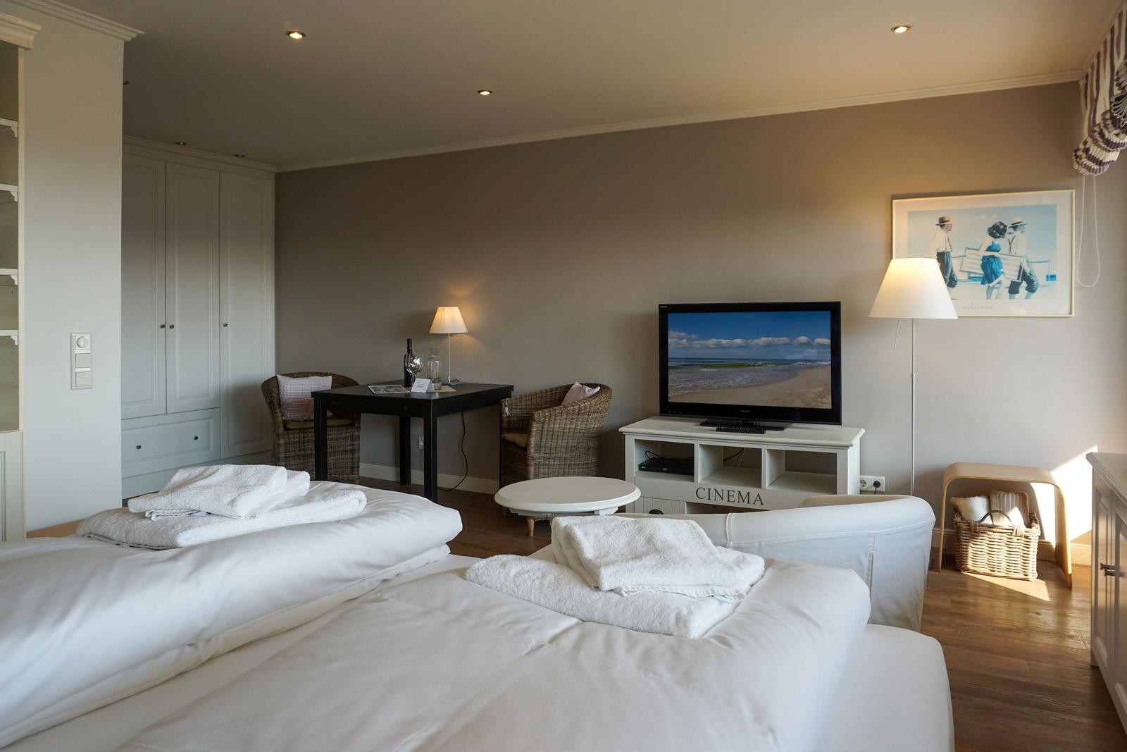 Zwei Betten mit weißen Laken, Fernseher und Sitzgelegenheiten im Zimmer.