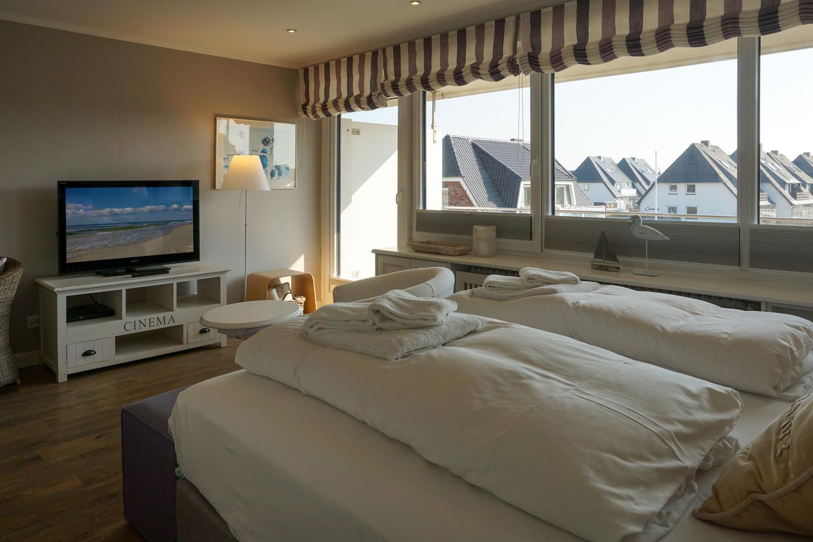 Zwei Betten mit weißen Bettwäsche, TV und Fenster mit Blick auf Dächer.