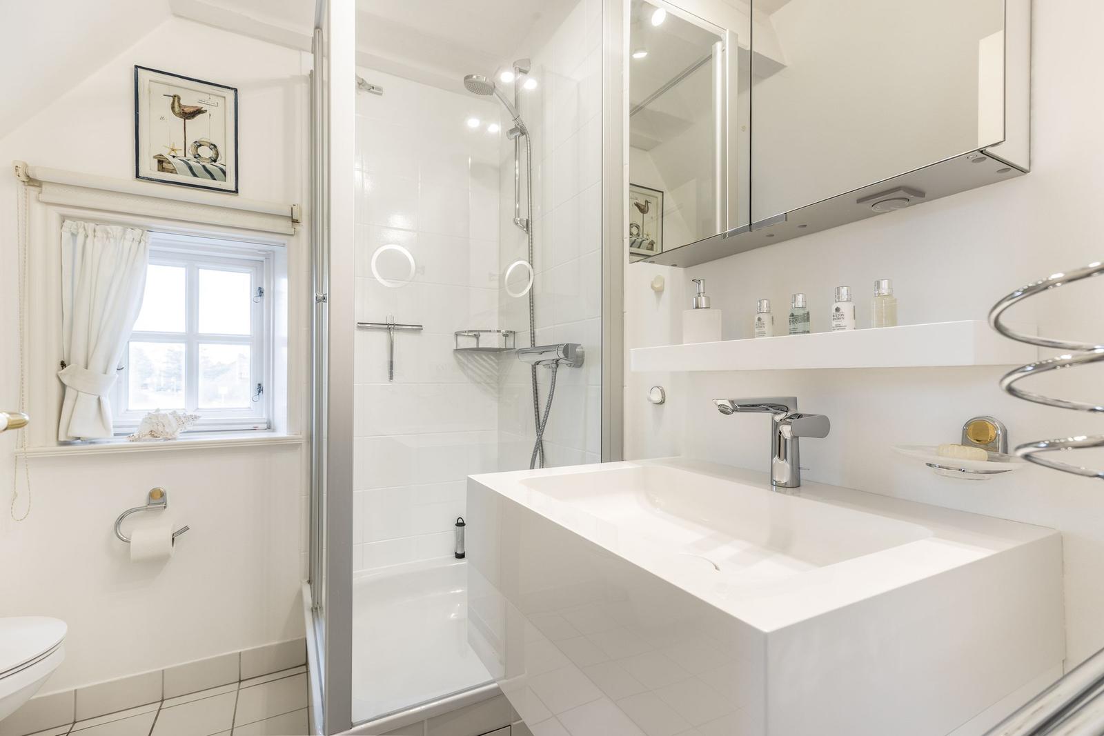 Badezimmer mit Dusche, Waschbecken und Fenster.