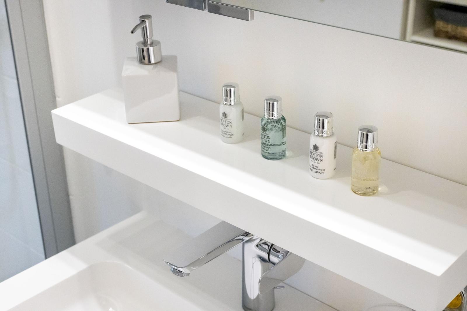 Badezimmer mit Waschbecken, Wasserhahn und Pflegeprodukten auf der Ablagefläche.