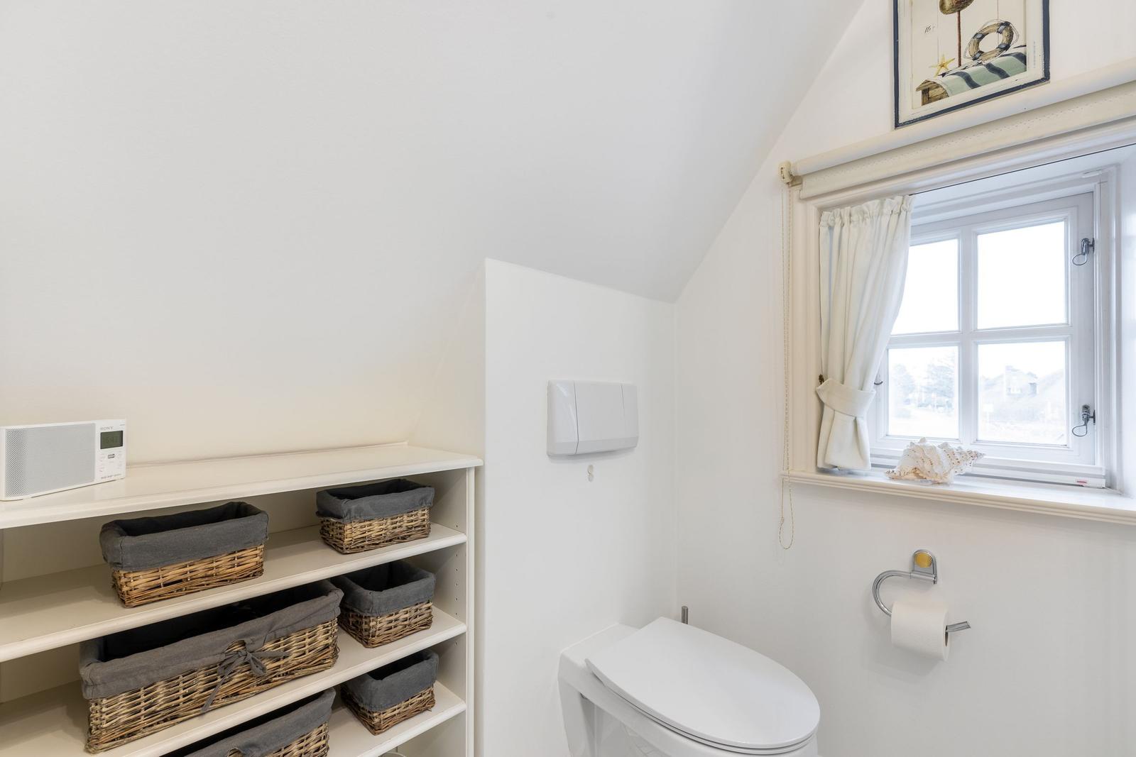 Badezimmer mit Toilette, Regal und Fenster mit Vorhang.