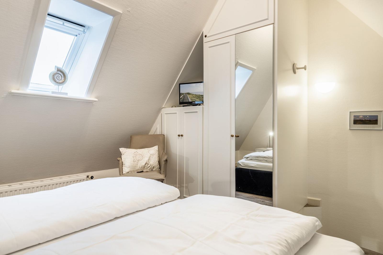 Schlafzimmer mit Dachfenster, Bett, Kleiderschrank und Fernseher.