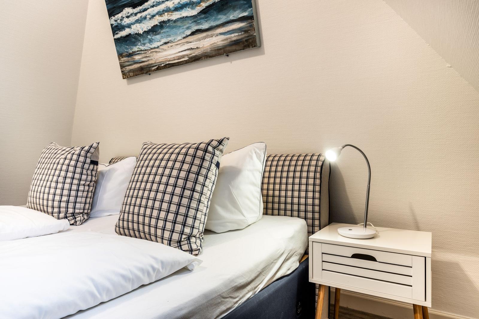 Schlafzimmer mit Bett, Kissen und Nachttisch mit Lampe.
