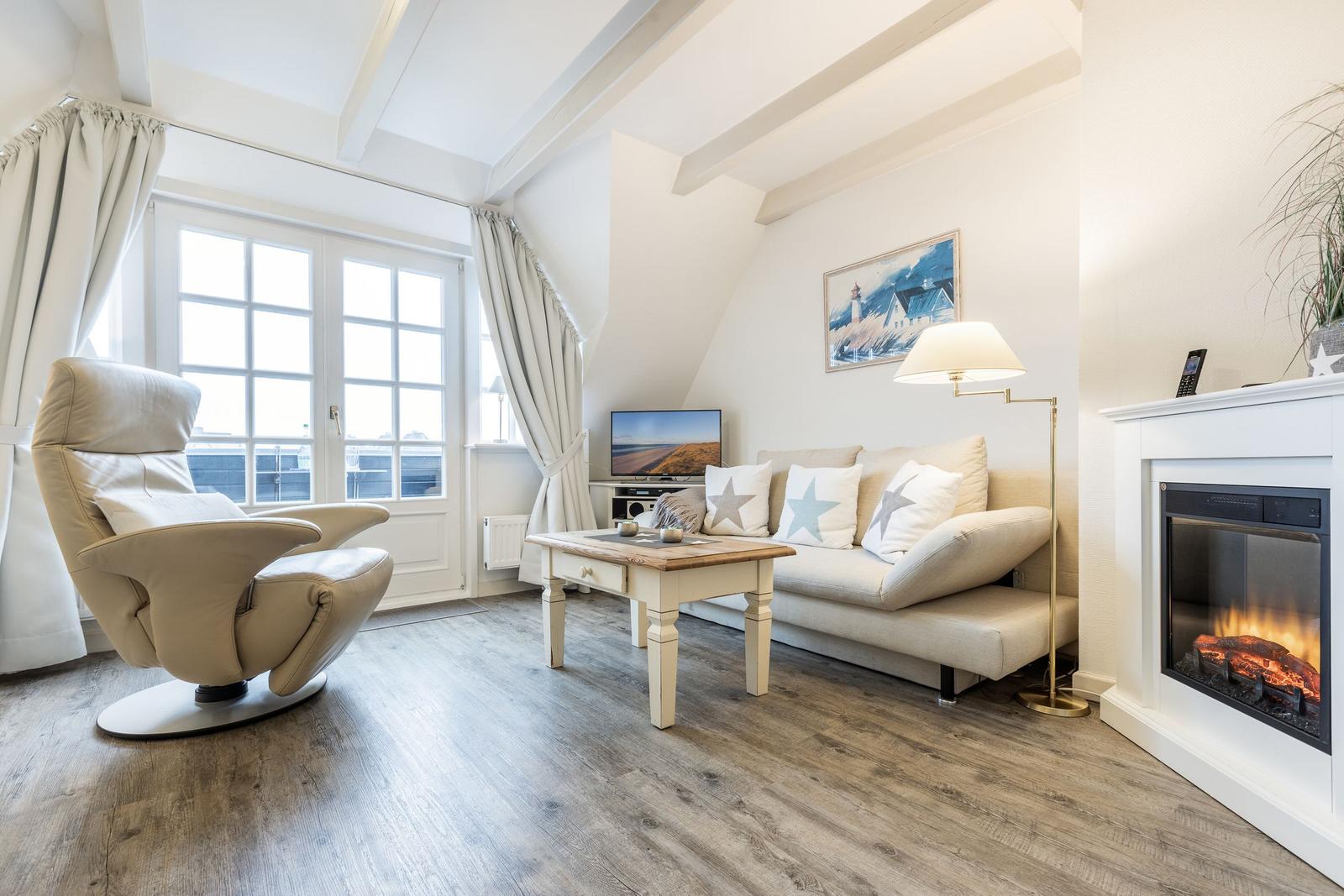 Wohnzimmer mit Sofa, Fernseher und Kamin. Holzfußboden und große Fenster.
