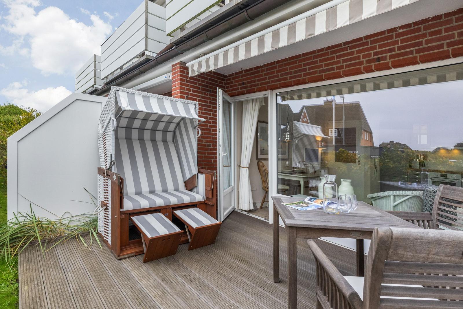 Terrace with beach chair, table, and chairs. Glass window leads to interior space.