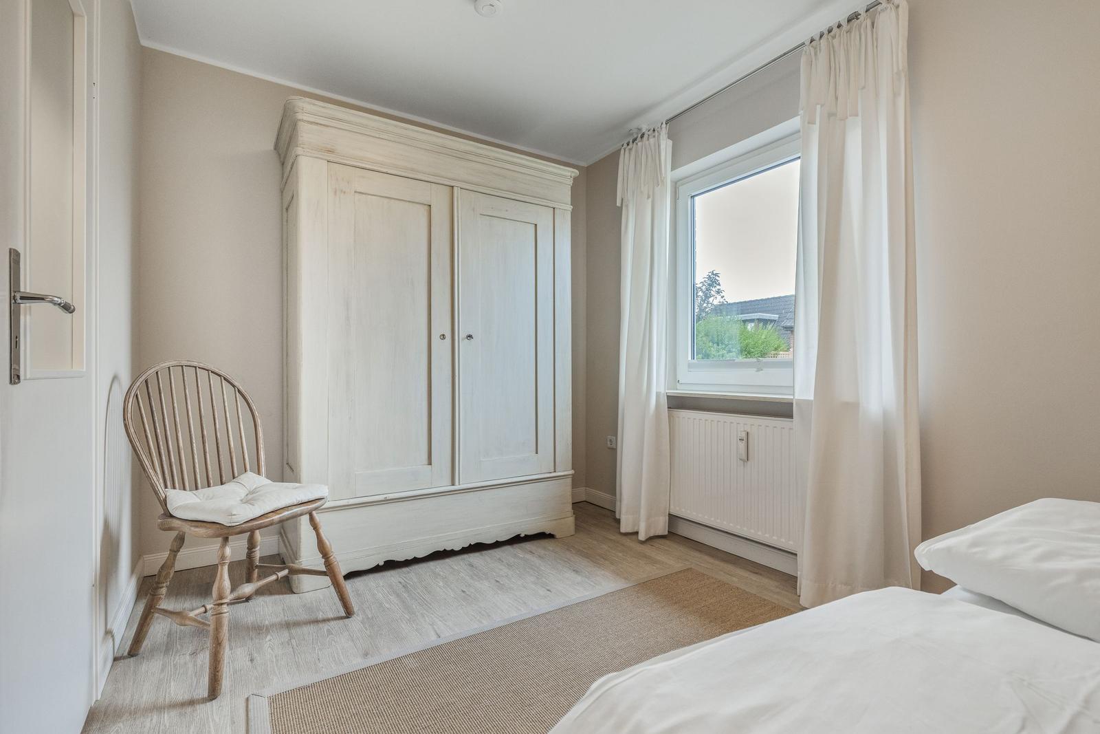 Bedroom with wardrobe, chair, and window with curtains.