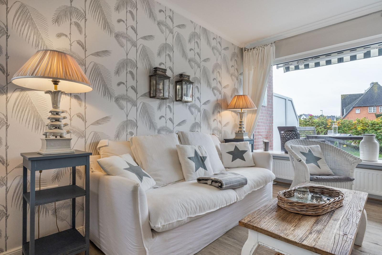 Living room with sofa, chair, and table. Wallpaper with palm leaves. View onto balcony.