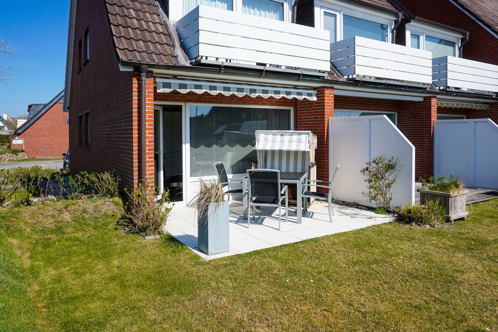 Terrace with seating and awning in front of a house with balcony.