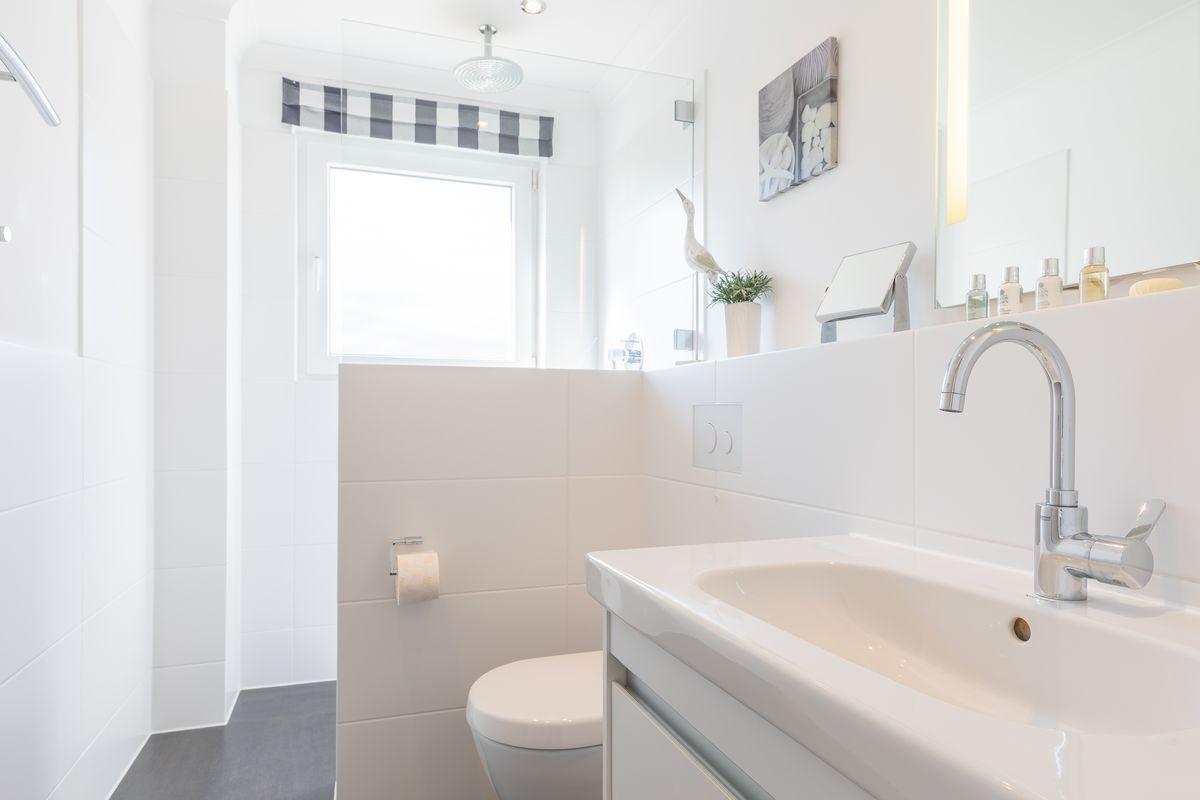 Bathroom with sink, toilet, and shower. Window with checkered curtain.