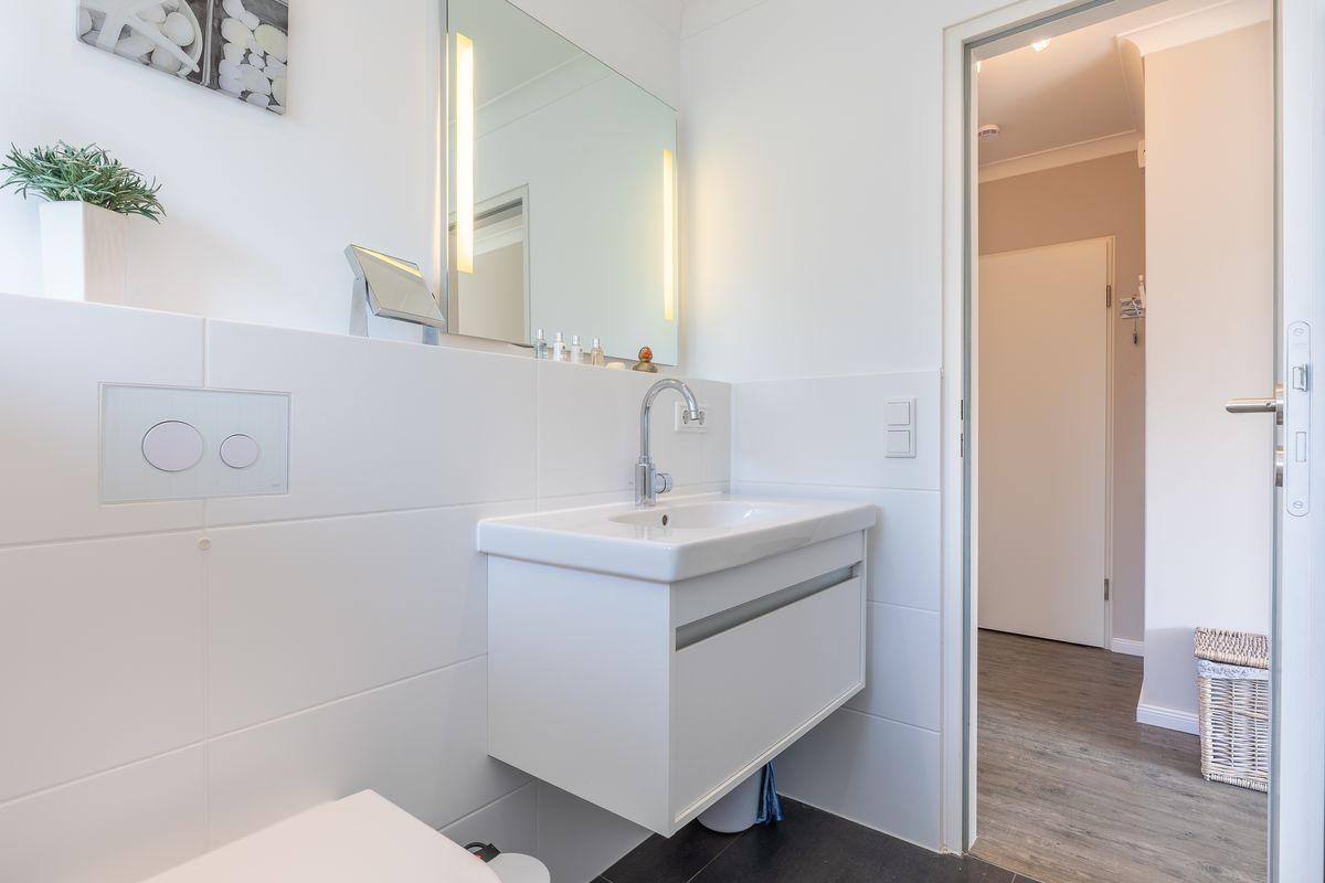 Bathroom with sink, mirror, and plant. Door leads to living area.