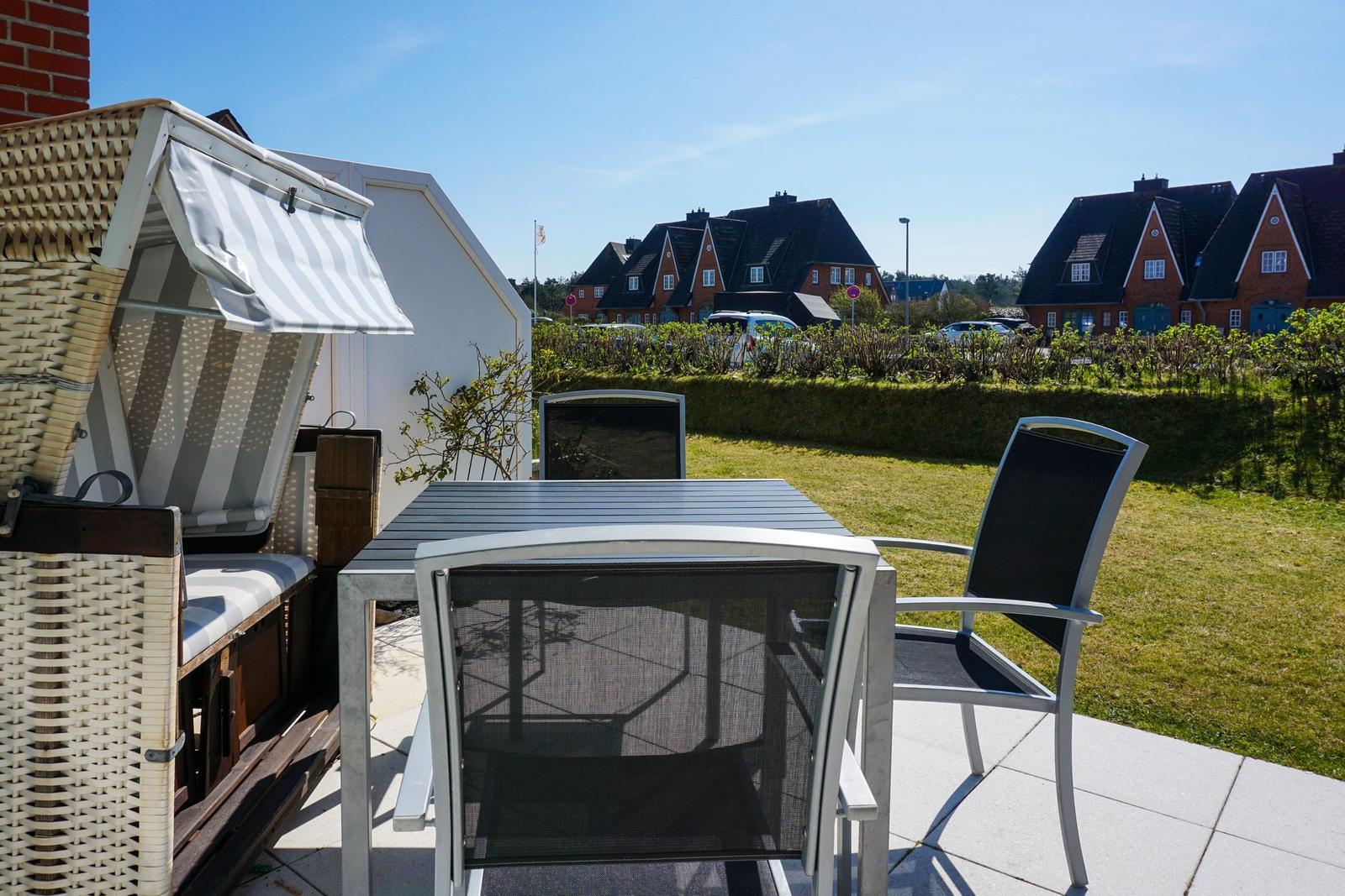 Terrace with table, chairs, and beach chair. View of lawn and houses.