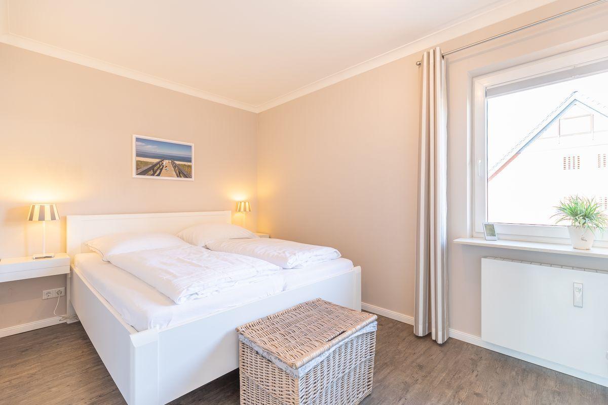 Bedroom with white bed, bedside lamps, and window with curtain.