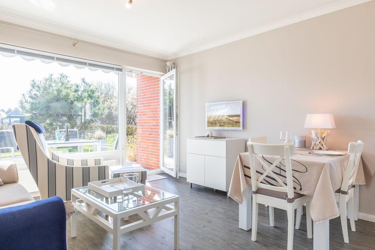 Living and dining area with table, chairs, and view to balcony.