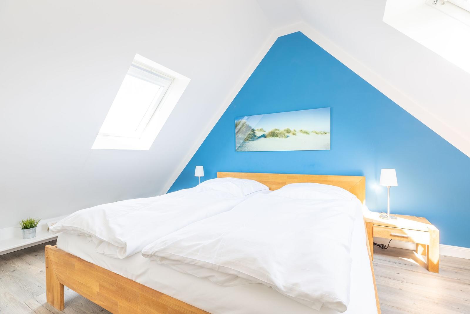 Schlafzimmer mit Dachschräge, blauer Wand, Holzbett und Dachfenster.