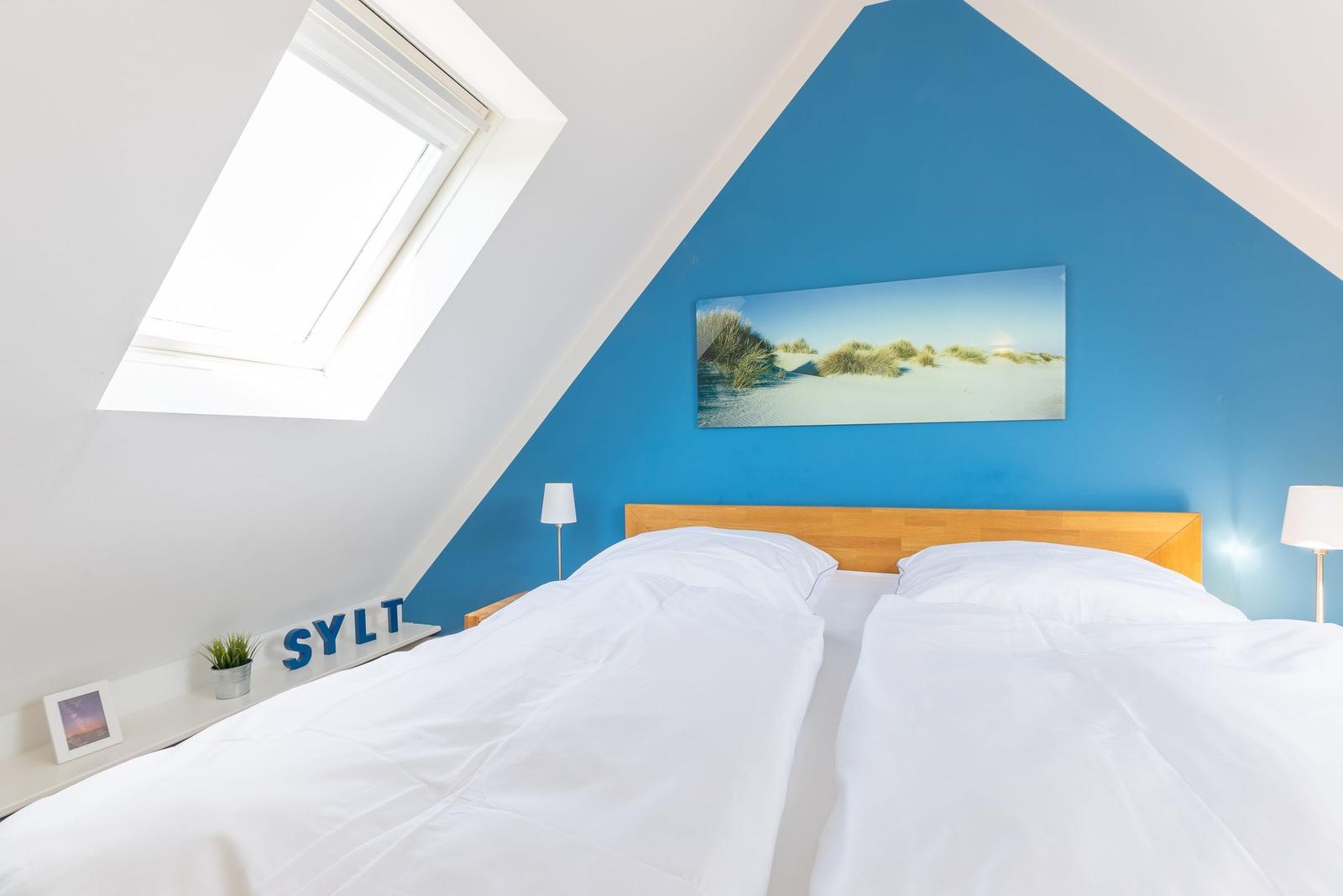 Schlafzimmer mit Dachschrägen, blauer Wand und Doppelschlafcouch.