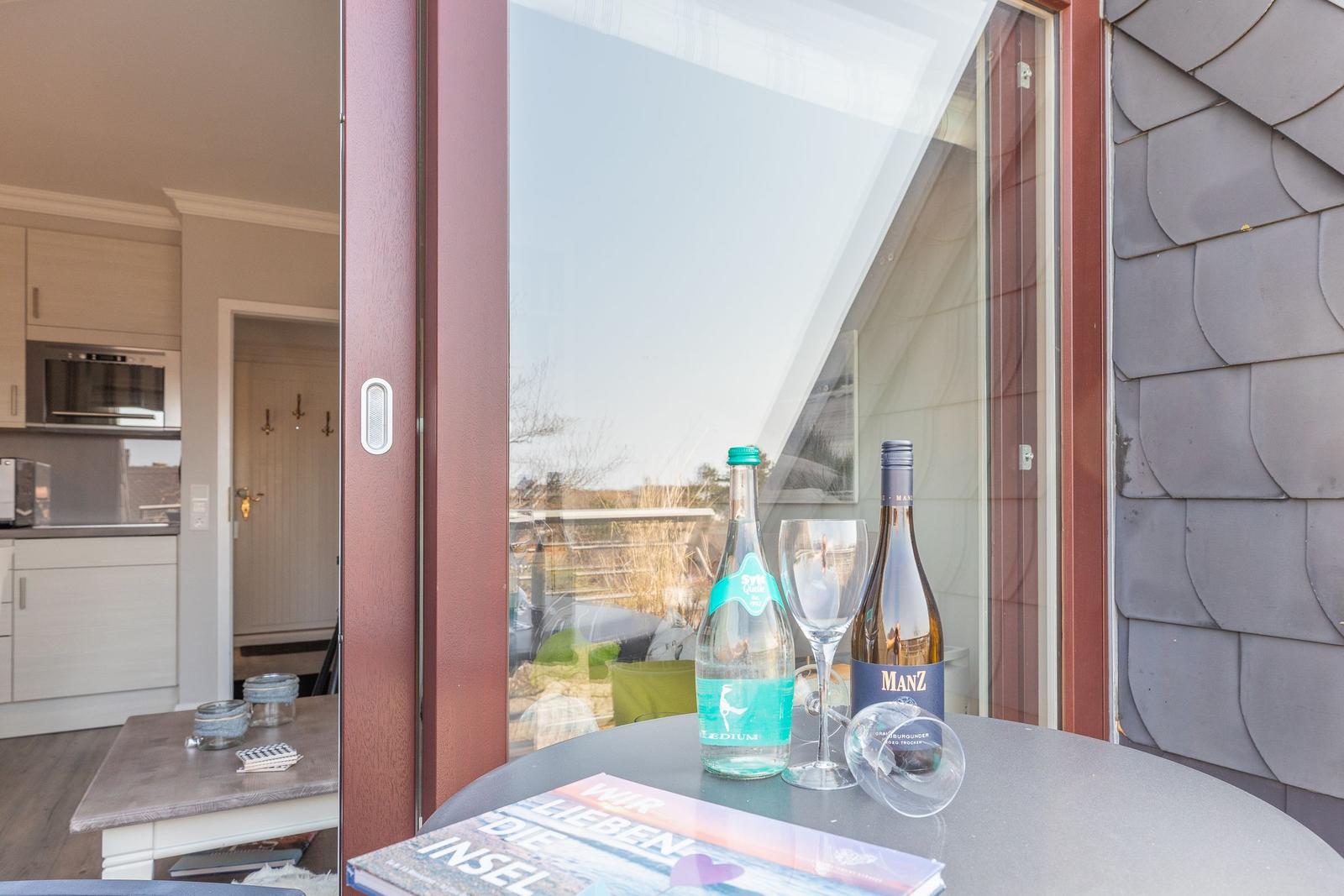 Tisch mit Wein und Wasser vor Terrassentür. Küche und Flur im Hintergrund.