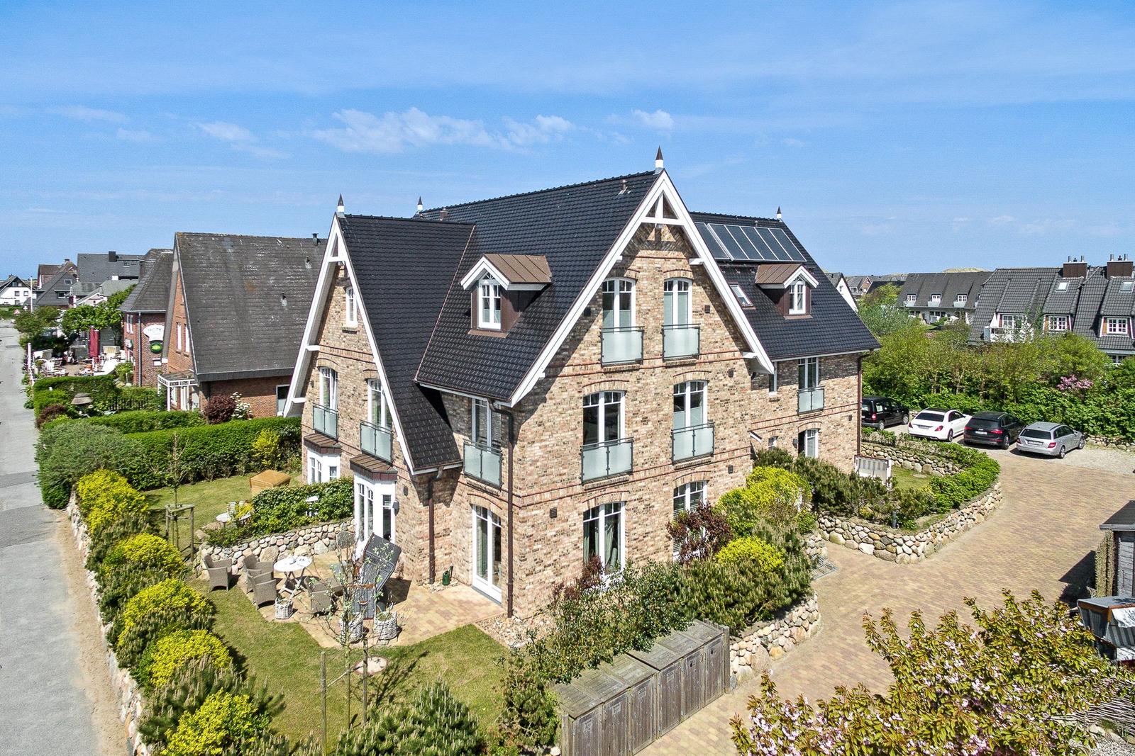 A large house with stone walls and dormer windows. Garden and parking area are visible.