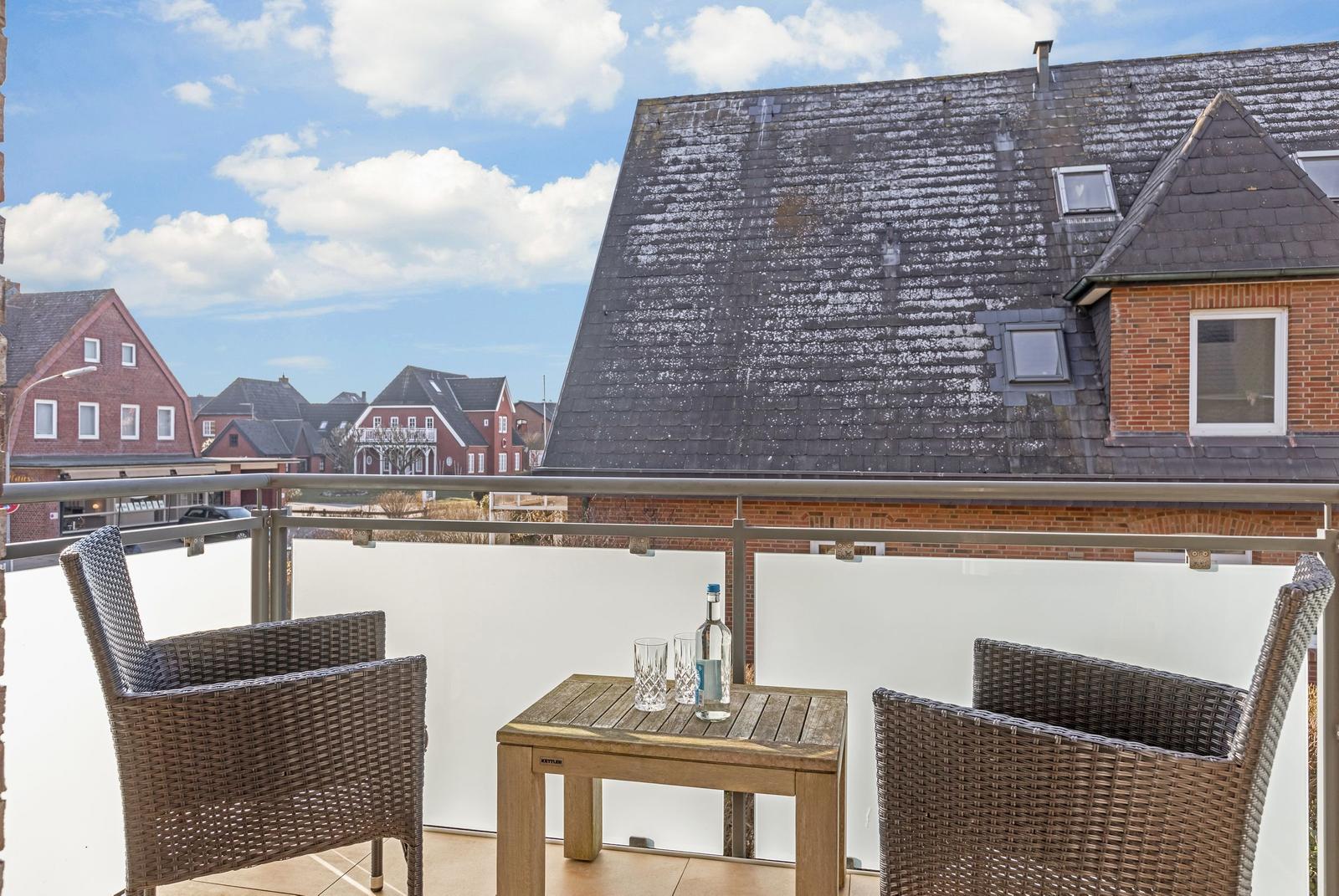 Terrace with table and two chairs, view of rooftops and street.