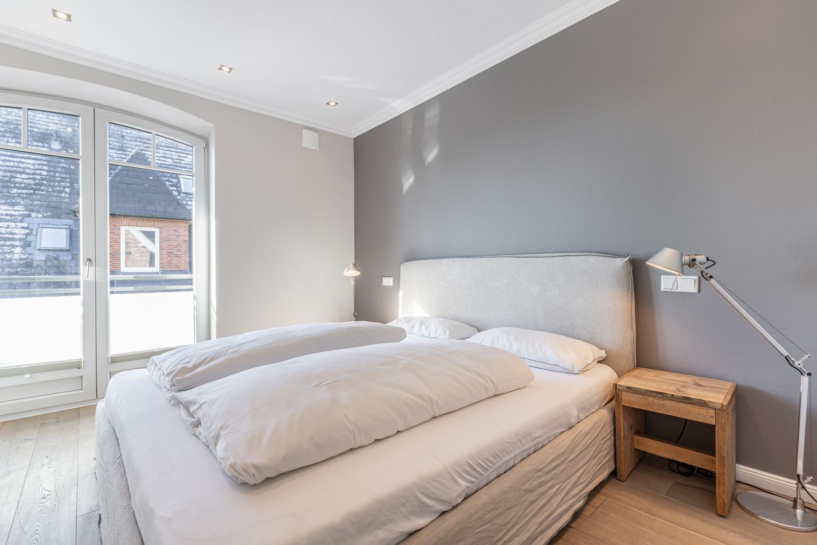 Bedroom with double bed, wooden side table, and window to balcony.