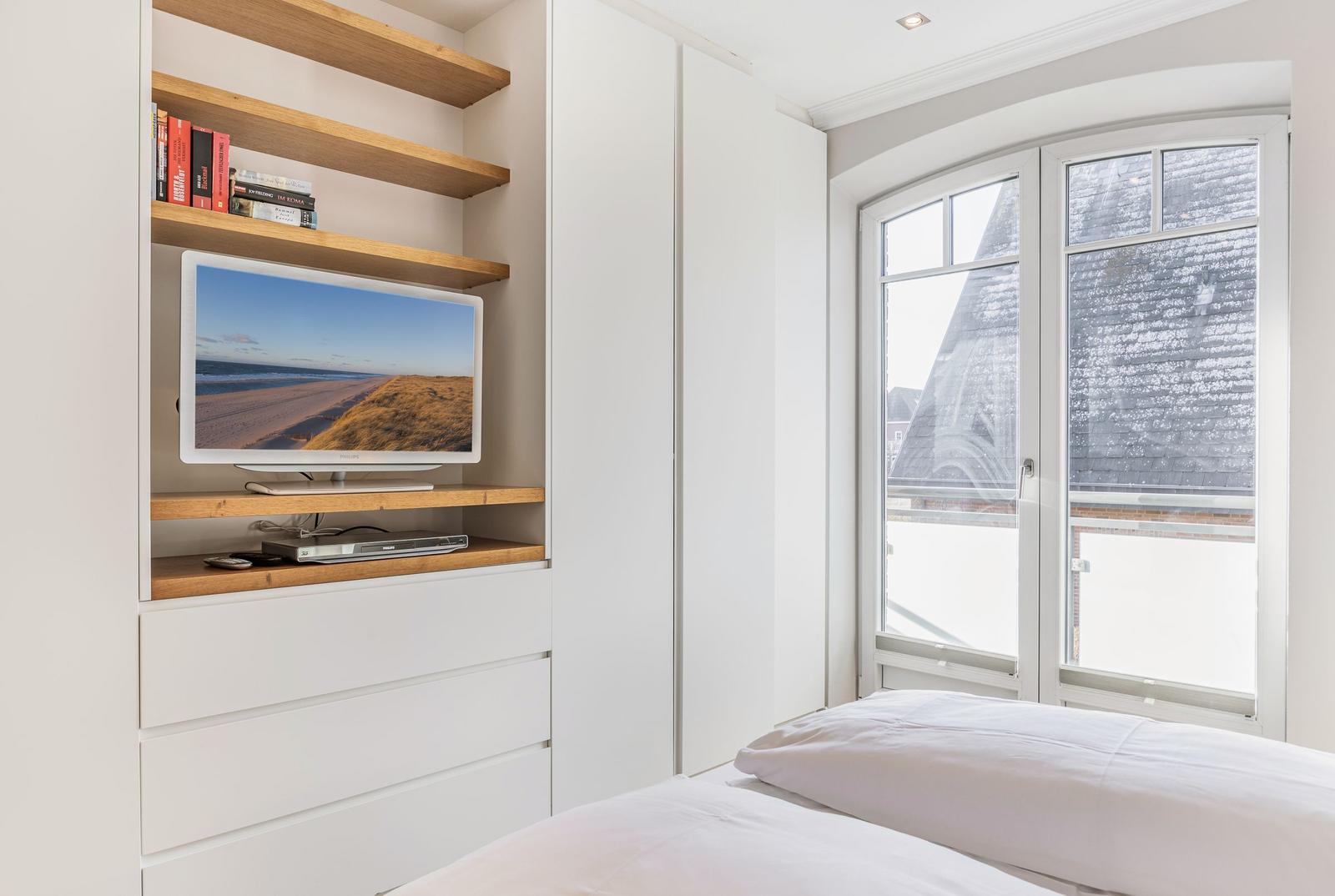 Bedroom with TV, bookshelf, and window view of roof