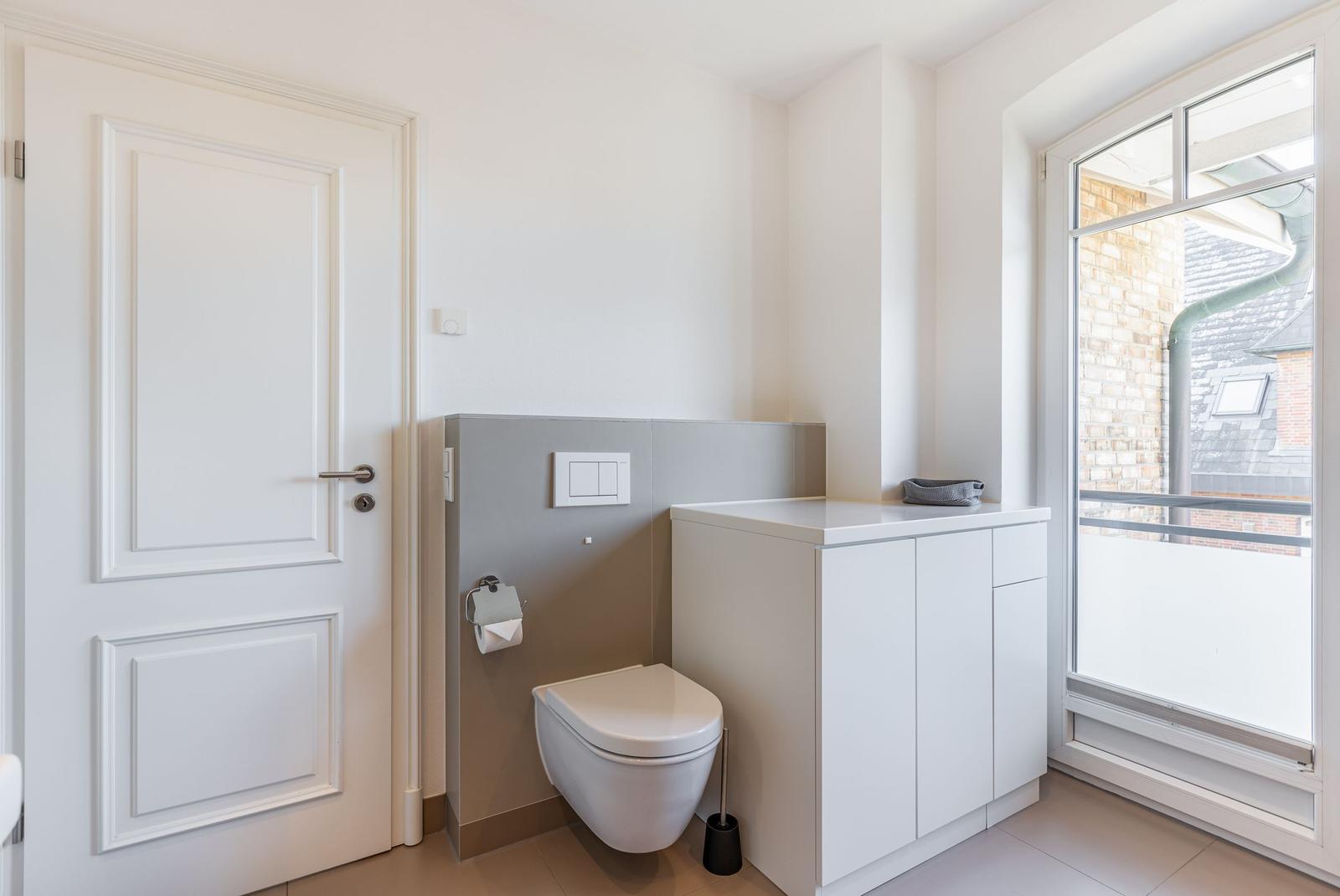 Toilet room with window, white door, and cabinet.