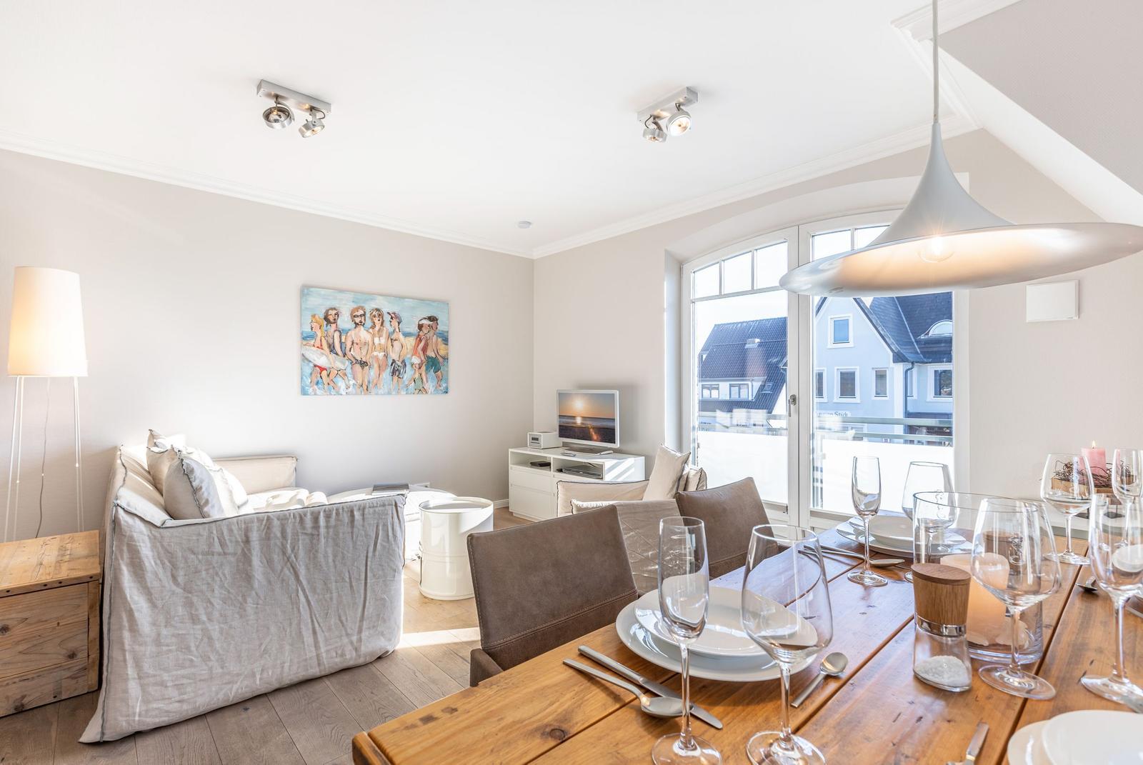 Dining room with wooden table and seating. Corridor to living room with TV.