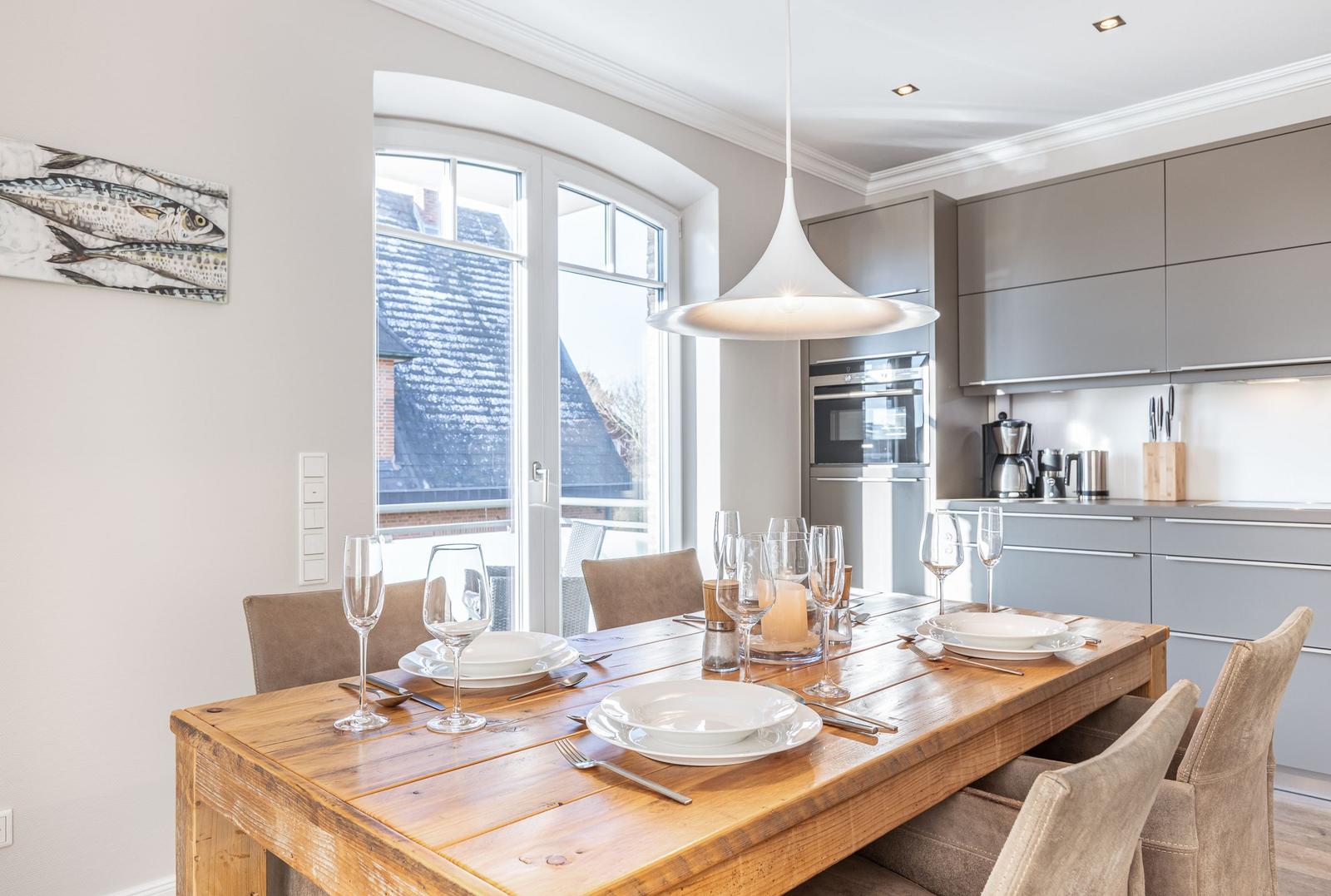 Dining area with wooden table and chairs. Kitchen with gray cabinets and window view.