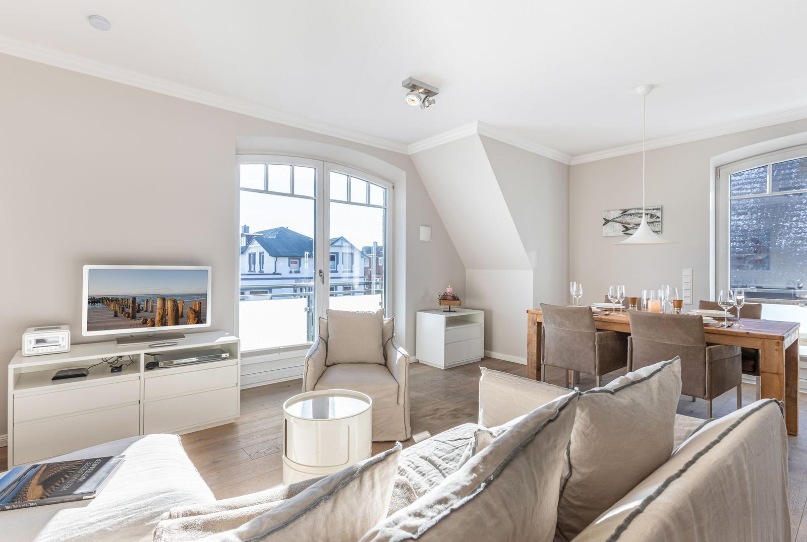 Living and dining area with TV, sofa, and table. View of the beach through windows.