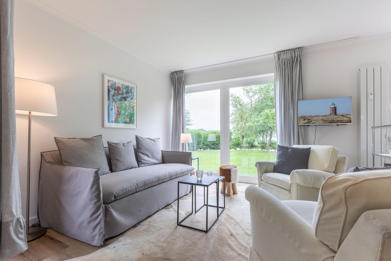 Living room with sofa, armchairs, and view of green area.