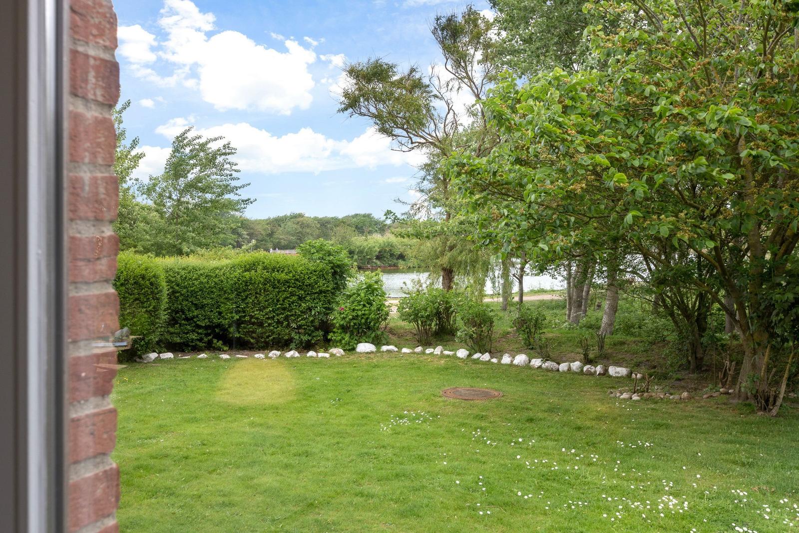 Green garden with stone border, trees, and view of a lake.