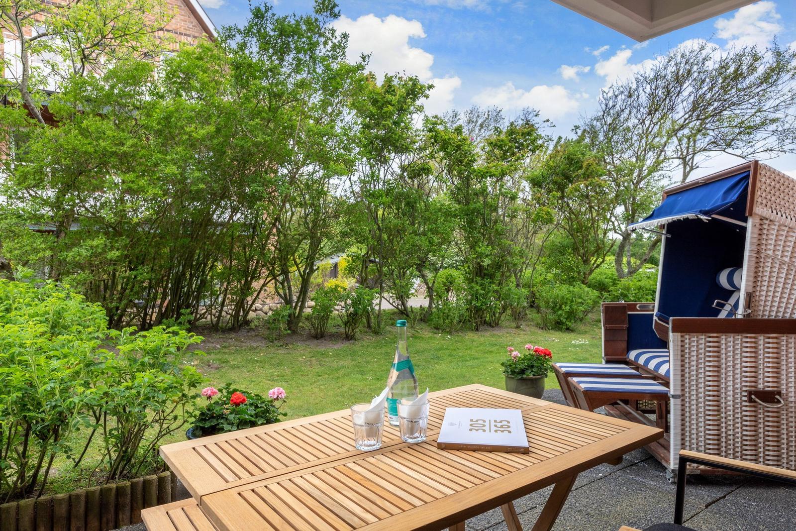 Terrace with table, lounge chair, and garden. Blue beach chair and green plants.