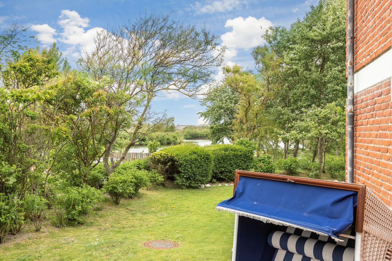 Garden with view of water and trees. Blue beach chair next to brick wall.