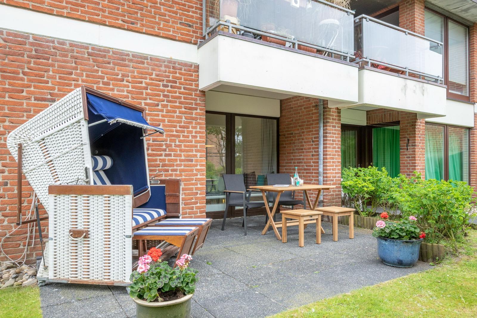 Terrace with beach chair, table, chairs, and plants in front of brick house.