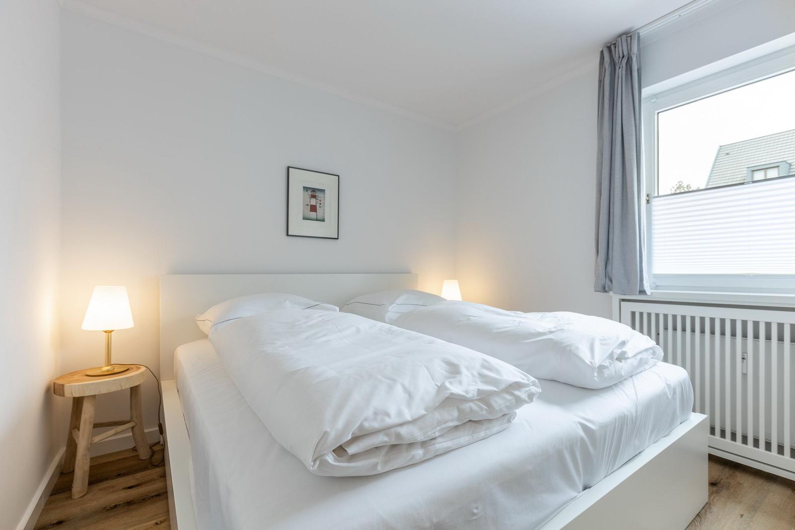 Bedroom with white bed, bedside table, and window.