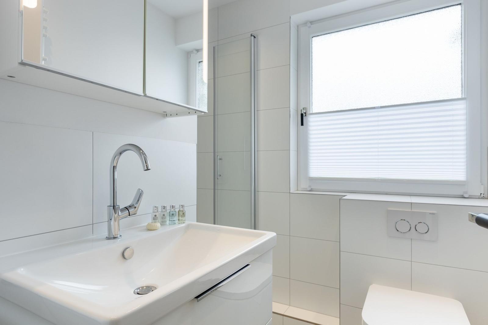 Bathroom with sink, shower, and window with blinds.