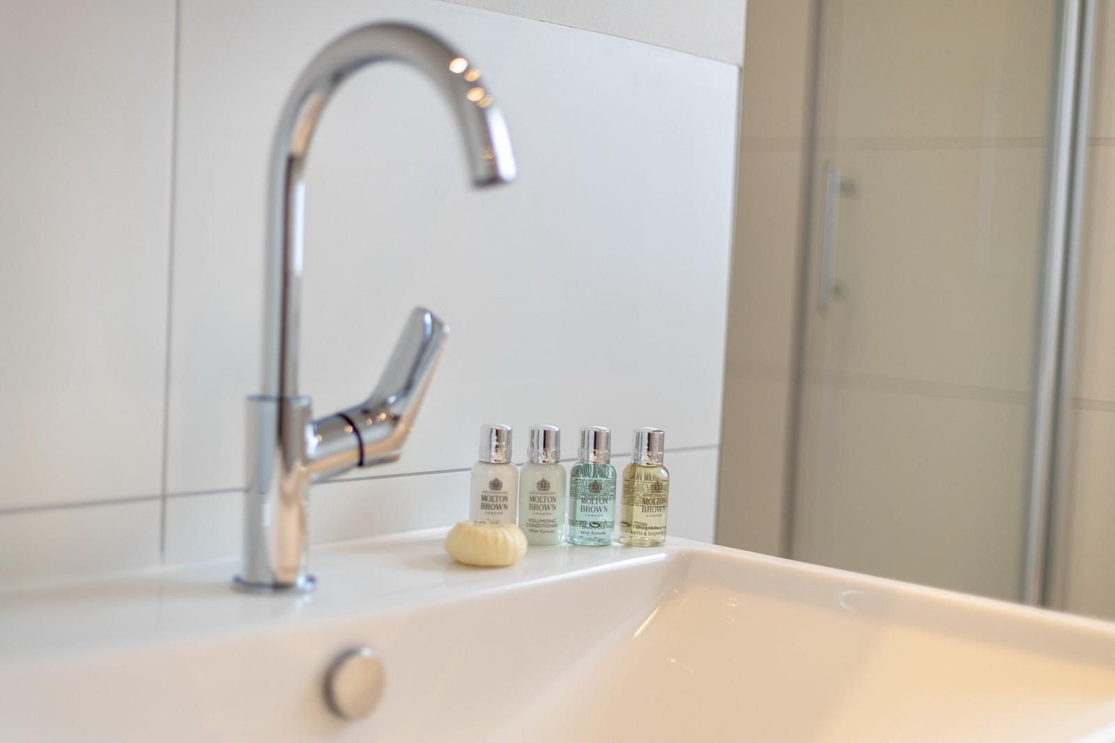 Sink with modern faucet and four bottles of toiletries.