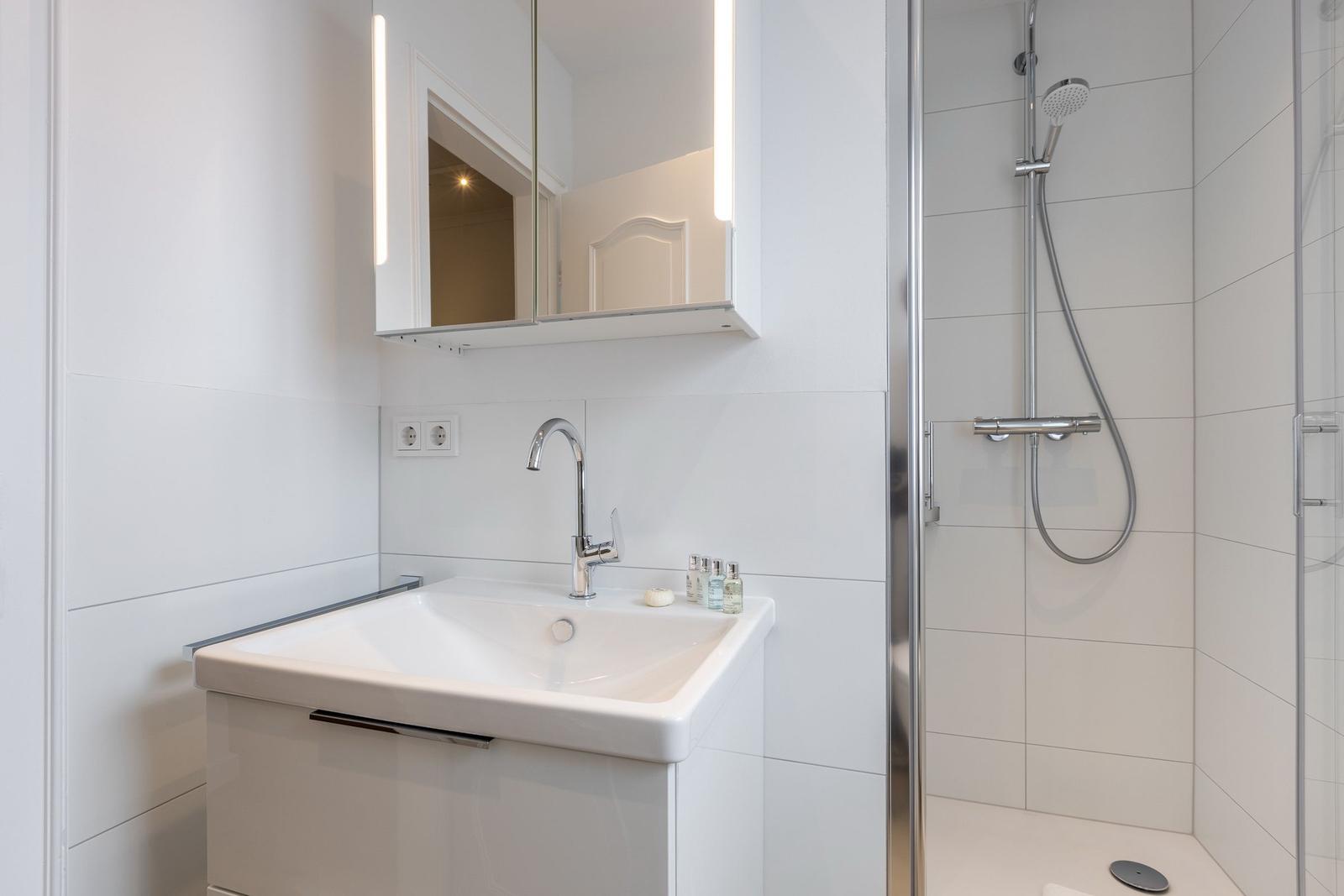 Bathroom with shower, sink, and lit mirror.