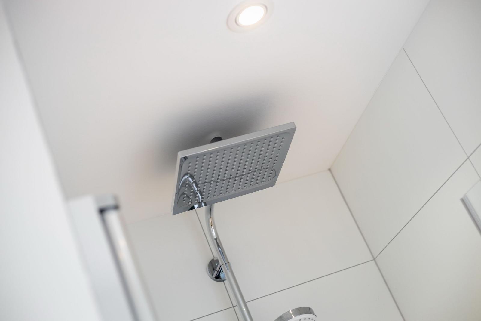 Shower area with ceiling-mounted showerhead and white tiles.