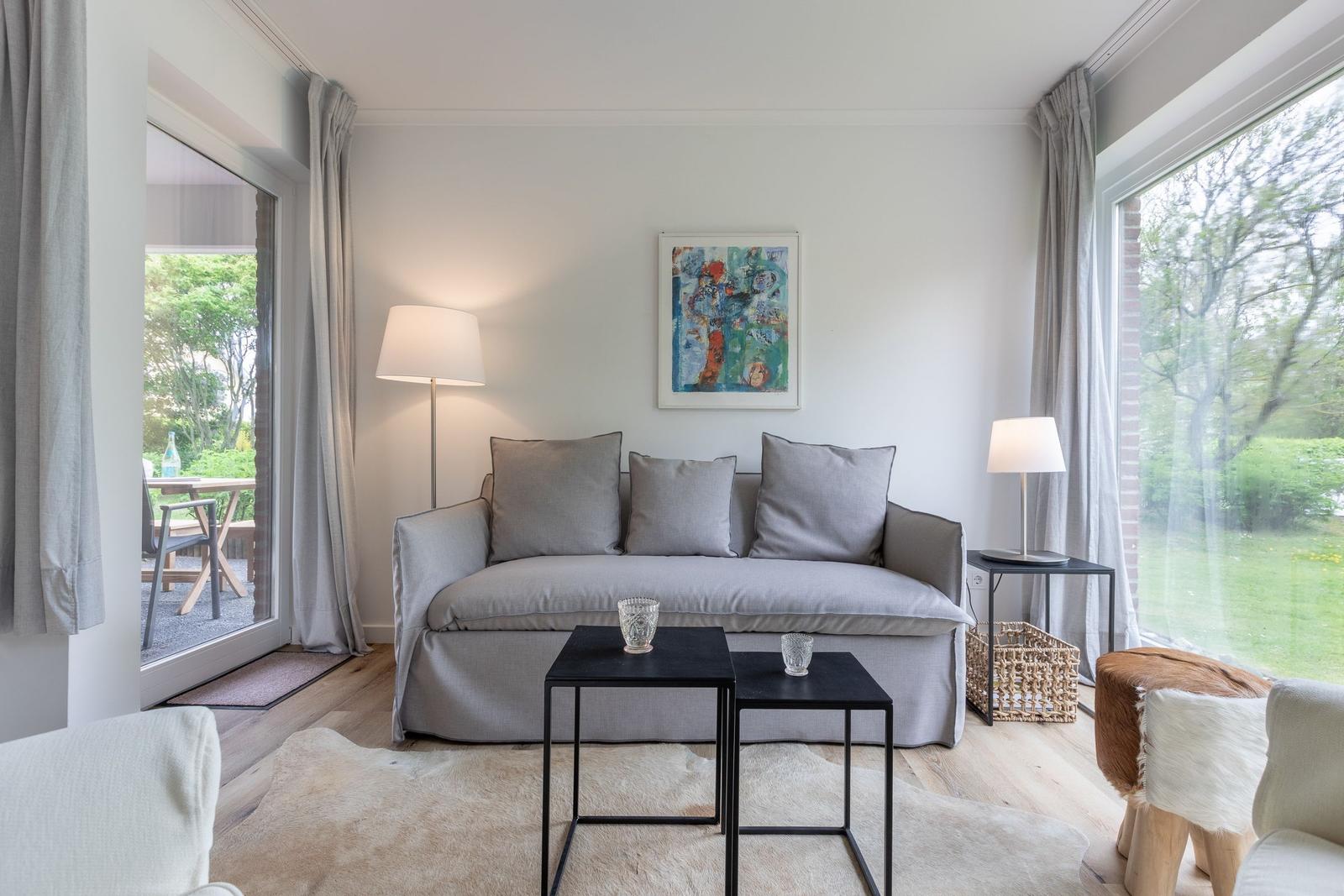 A living room with gray sofa, two tables, and view of garden.