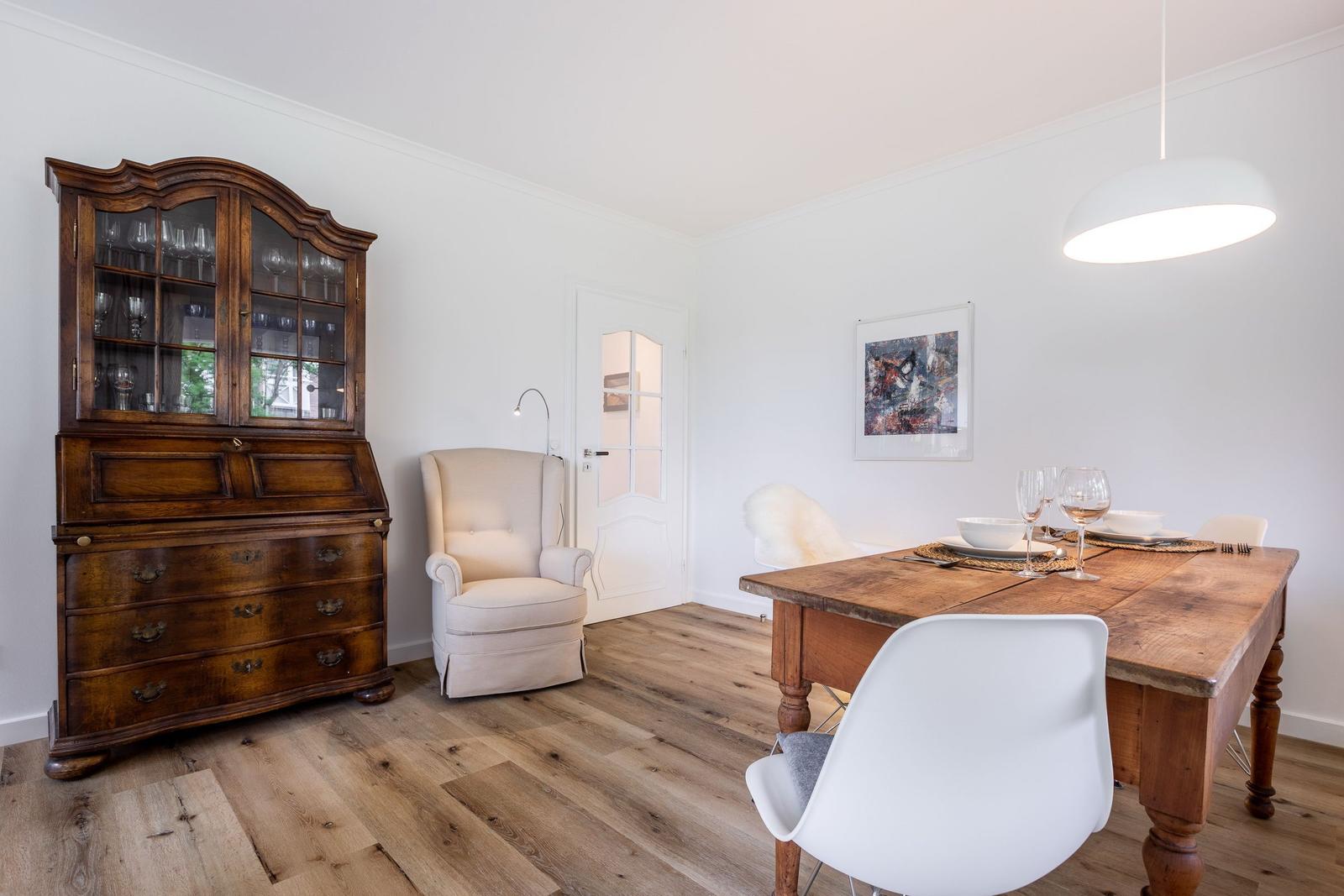 Dining room with wooden table, chairs, and antique cabinet. White walls and wooden floor.