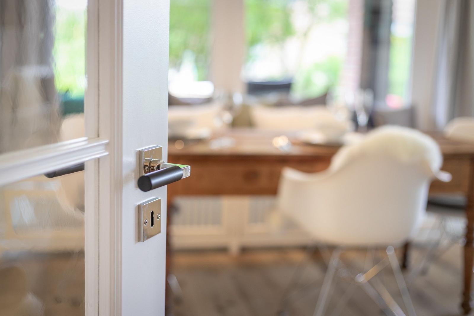 Door handle leads to dining room with wooden table and chairs.