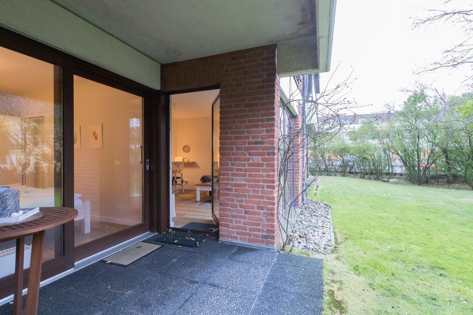Entrance with glass doors leading to living area. Outdoor space with lawn and stone wall.