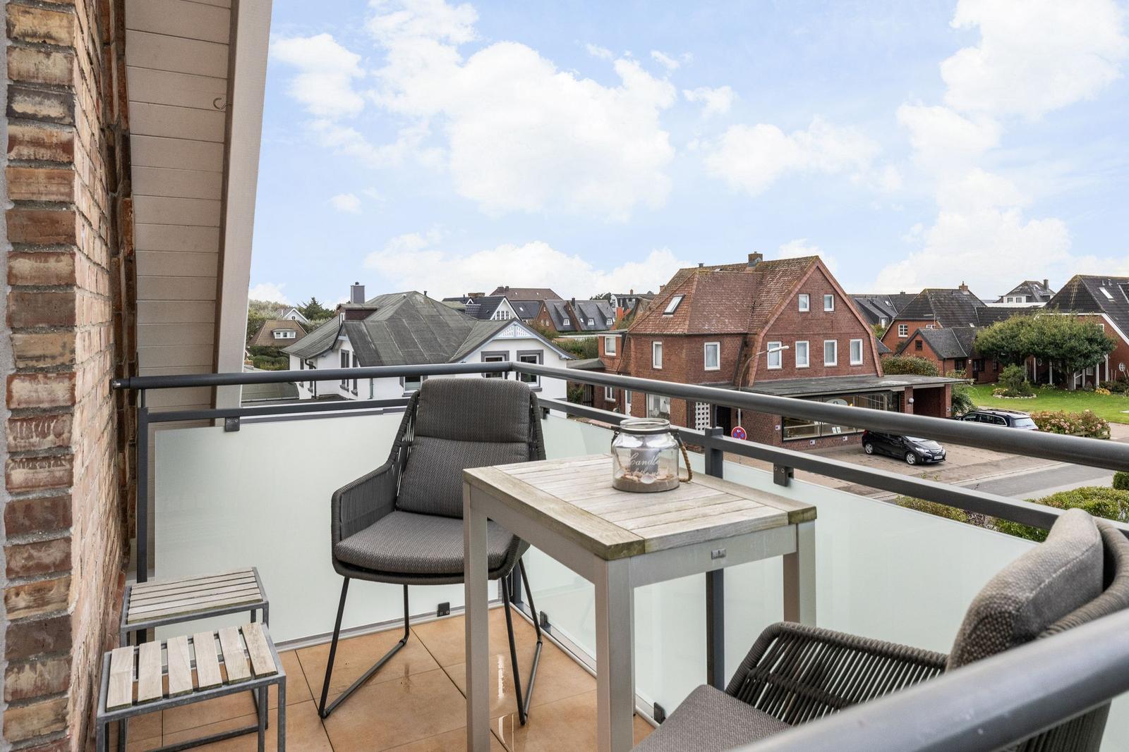 Balkon mit Tisch und Stühlen, Blick auf Wohnhäuser und Straße.
