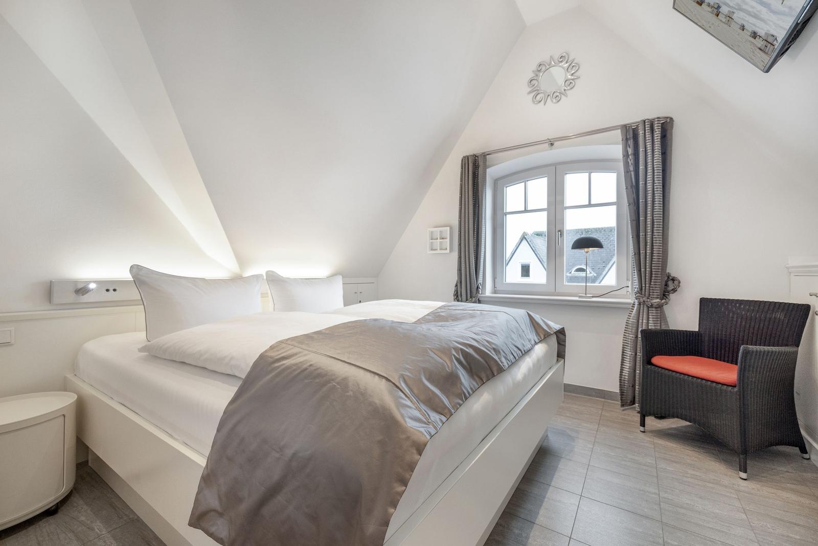 Schlafzimmer mit Doppelbett, Fenster und Sessel.