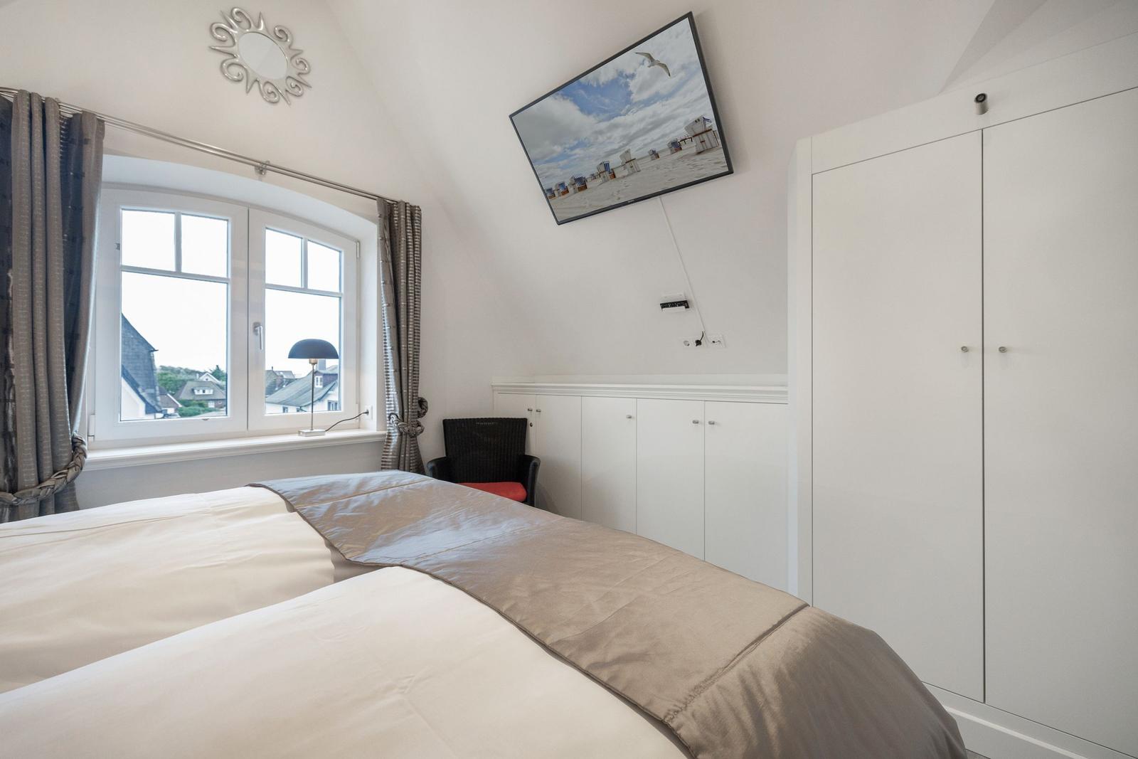 Schlafzimmer mit Bett, Fenster und Kleiderschrank. Wandbild zeigt Strand.