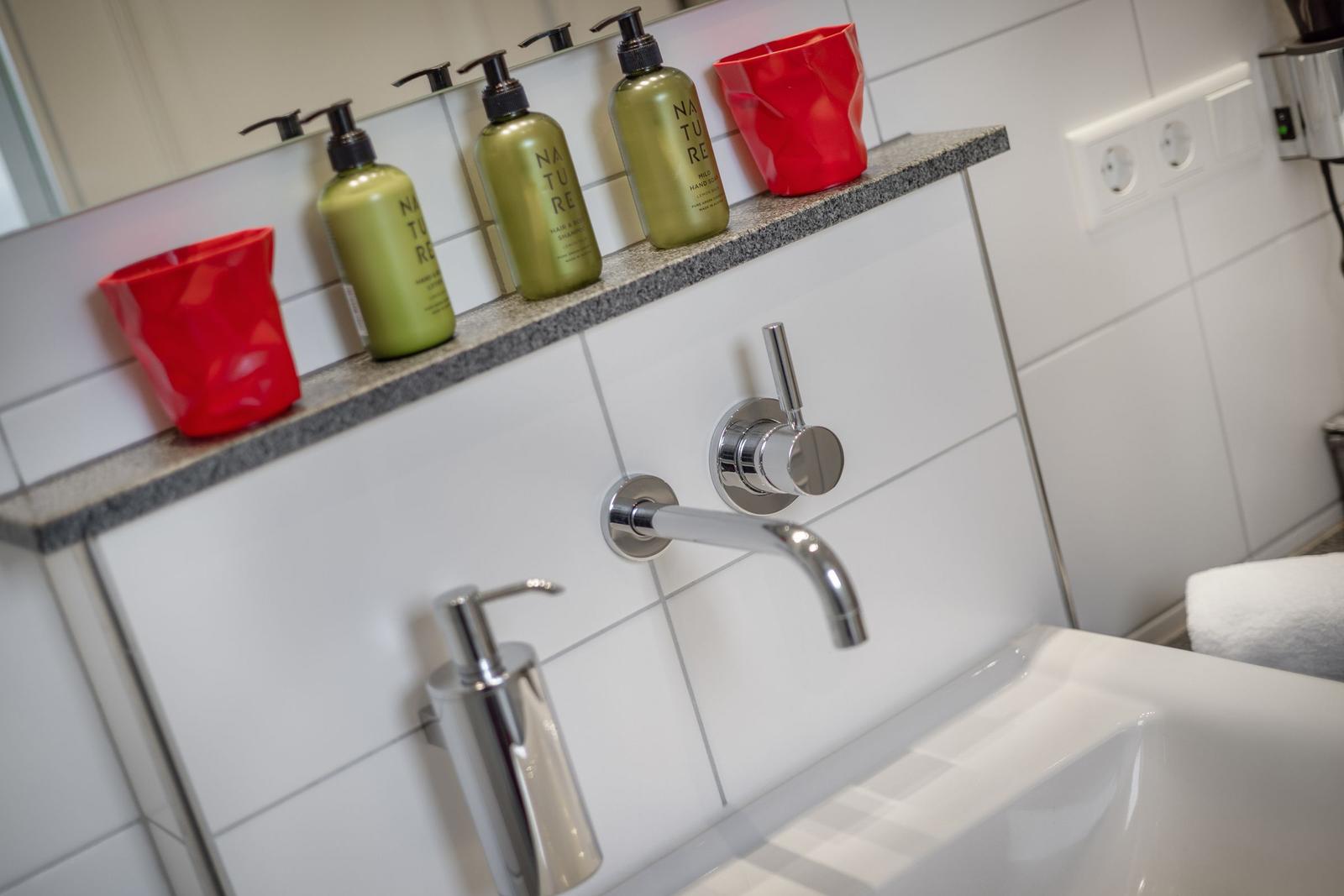 Badezimmer mit Waschbecken, Wasserhahn und Pflegeprodukten auf Arbeitsplatte.
