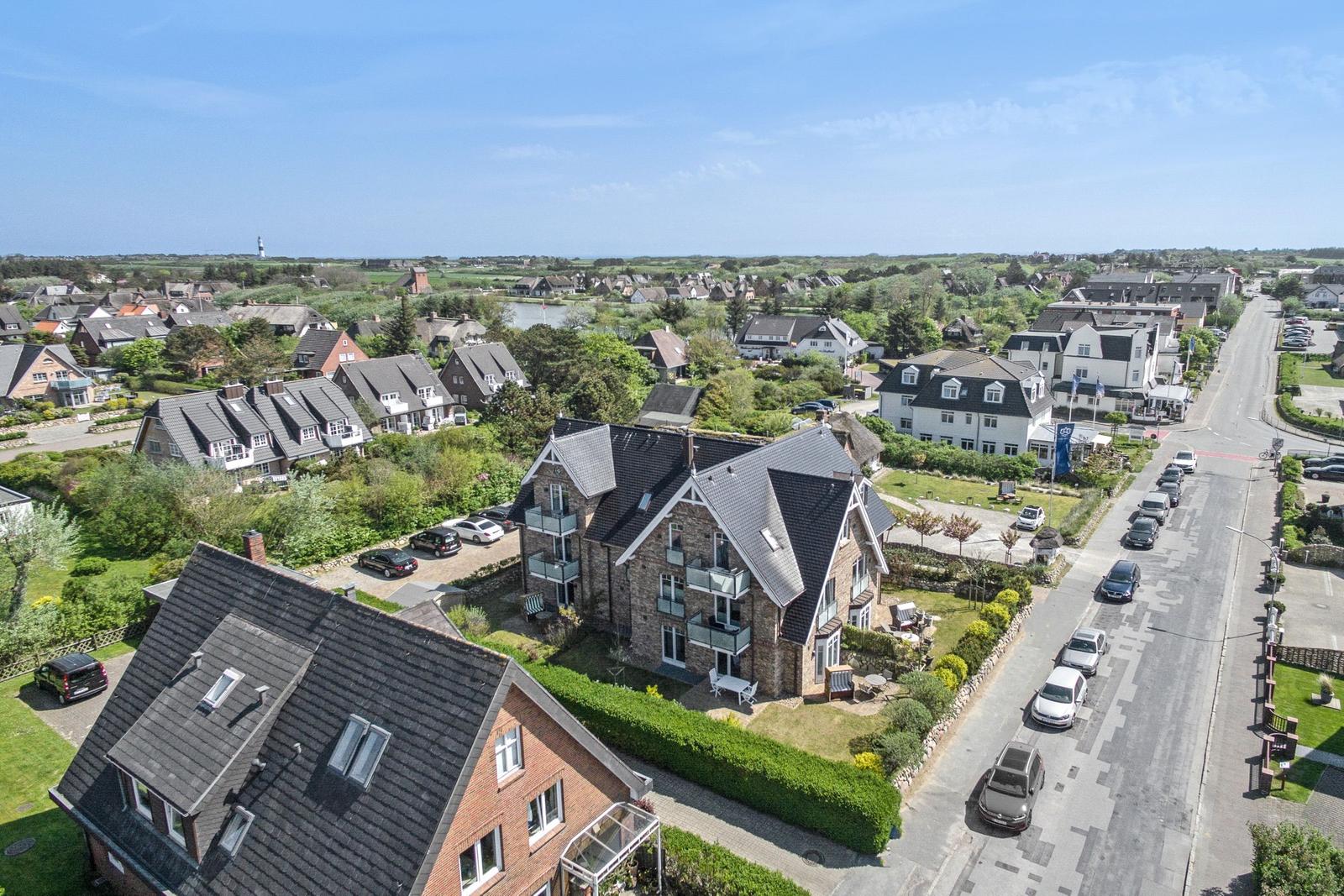 Haus mit Balkon, umgeben von Grünflächen und Straße mit geparkten Autos.